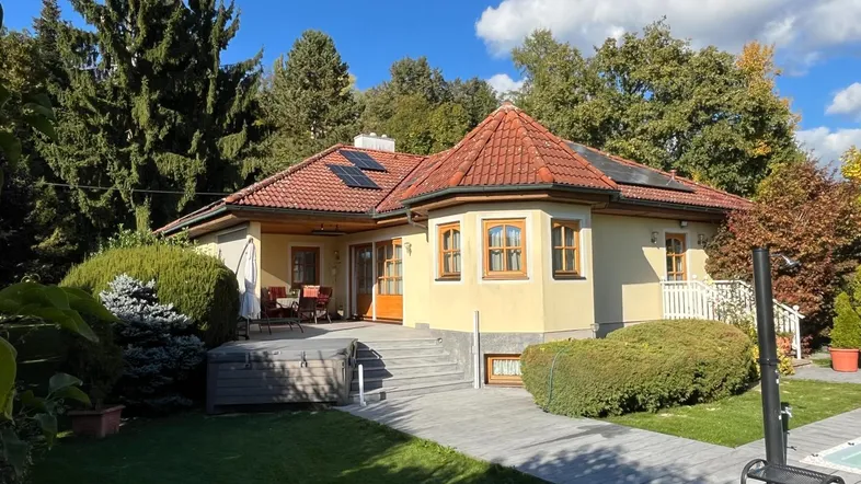 Charmantes Einfamilienhaus mit rotem Ziegeldach, Sonnenterrasse und gepflegtem Garten unter blauem Himmel.