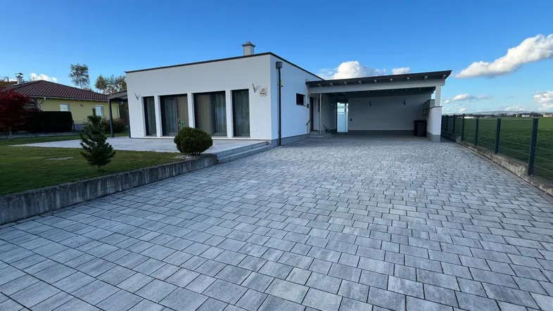 Moderne Einfamilienhausfassade mit gepflasterter Auffahrt und Carport unter blauem Himmel.