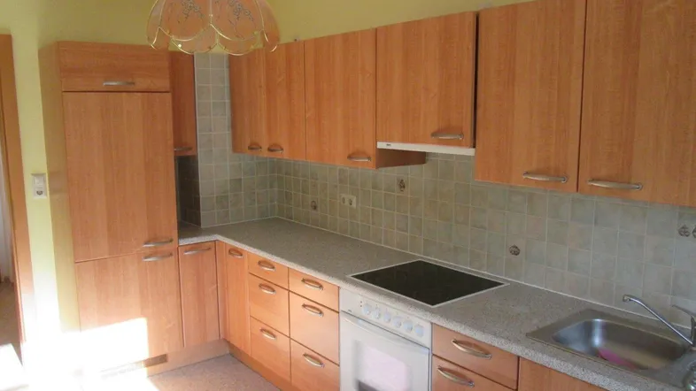 Funktionale Küche mit Holzschränken, hellen Fliesen und integrierten Geräten.