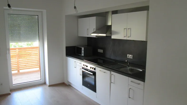 Moderne Küchenzeile mit weißen Schränken, dunkler Arbeitsplatte und Zugang zu einem Balkon.