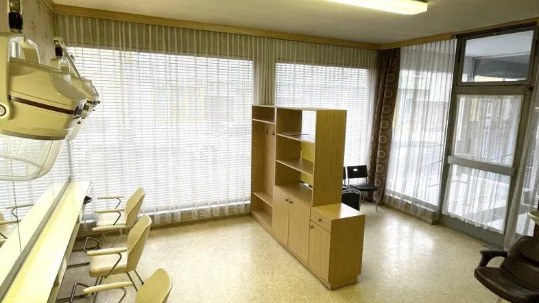 Geräumiger Innenraum eines Friseursalons mit mehreren Arbeitsplätzen, großen Fenstern und Jalousien, gut beleuchtet.