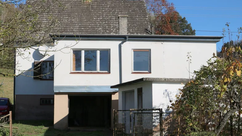Rückseite des Hauses mit Garageneinfahrt und Blick auf bewaldete Hügel.