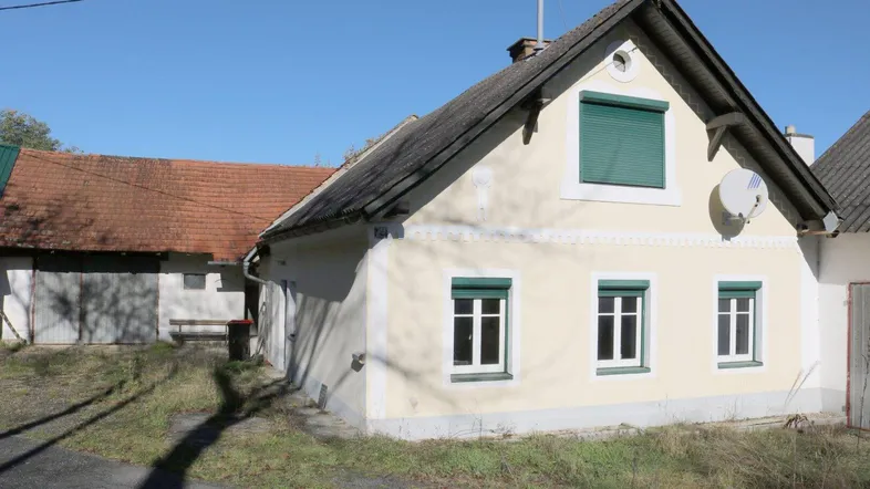 Traditionelles Landhaus mit gelber Fassade, grünen Fensterläden und Satteldach in ländlicher Umgebung.