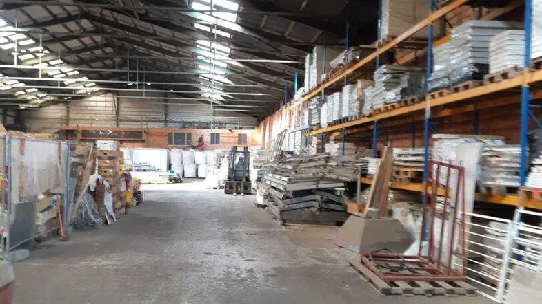 Geräumige Lagerhalle mit hohen Decken, Oberlichtern und Regalen für die Warenlagerung.