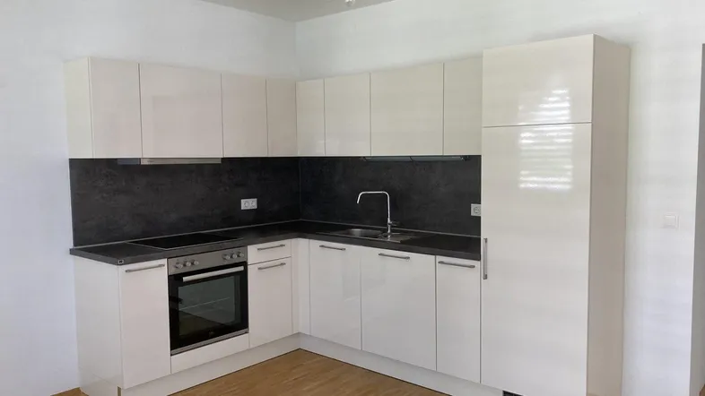 Moderne Einbauküche in hellem Design mit glänzenden Fronten und dunkler Arbeitsplatte.
