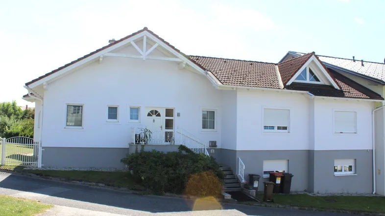 Rückseite des Hauses mit großer Terrasse, Garten und üppiger Bepflanzung, die Privatsphäre bietet.