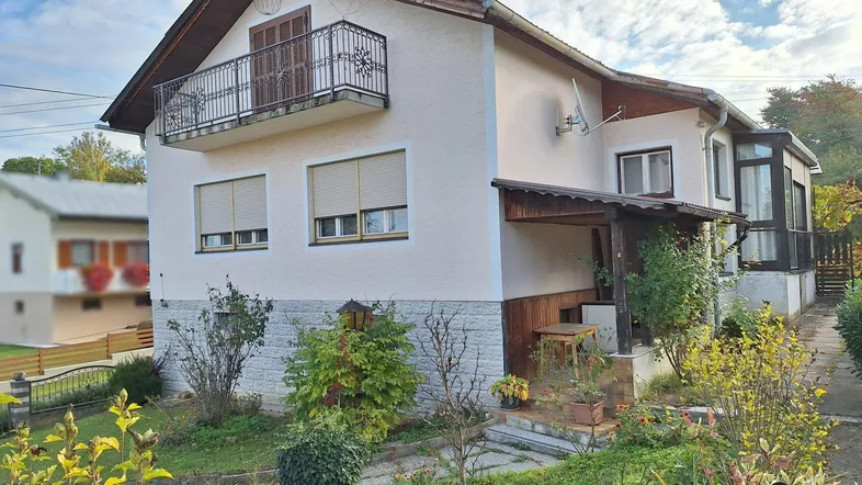 Seitenansicht des Hauses mit Balkon, überdachtem Sitzbereich und Garten.