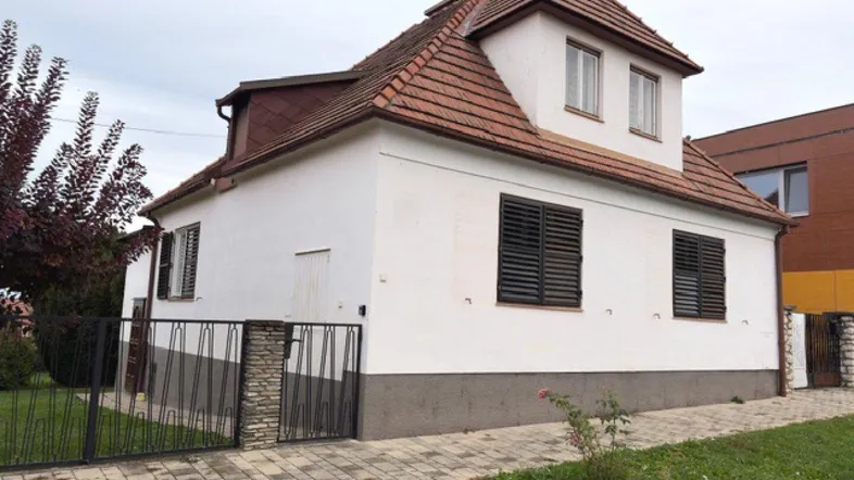 Weißes Einfamilienhaus mit braunem Ziegeldach, schwarzen Fensterläden und gepflasterter Einfahrt.