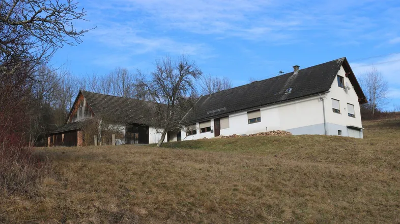 Ländliches Anwesen mit Wohnhaus und Scheune auf einem Hügel unter blauem Himmel.