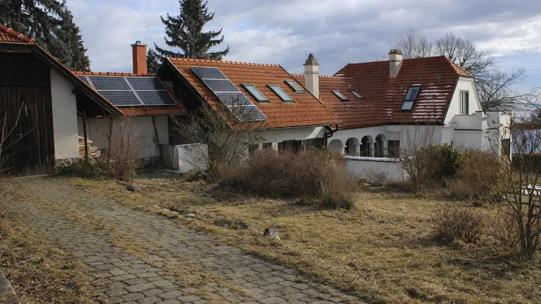 Hausfassade mit Ziegeldach, Solarpaneelen und einem gepflasterten Weg, umgeben von einem naturbelassenen Garten.