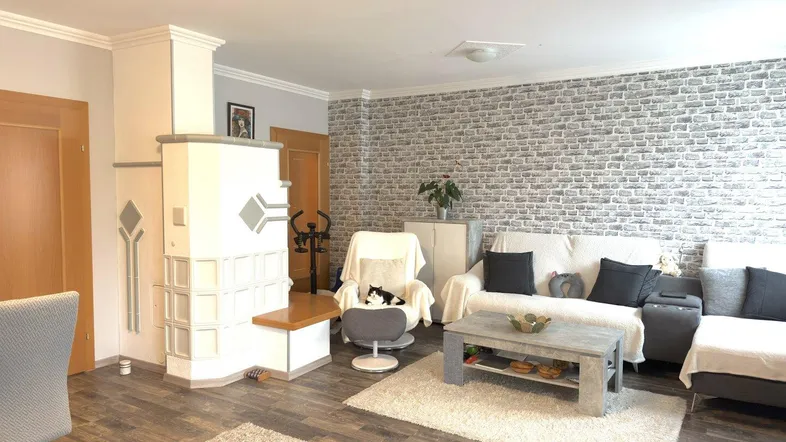 Gemütliches Wohnzimmer mit modernem Kaminofen, Holzboden und einer Akzentwand in Ziegeloptik.