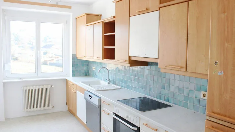 Helle Küche mit Holzschränken, blauen Fliesen und integrierten Geräten.