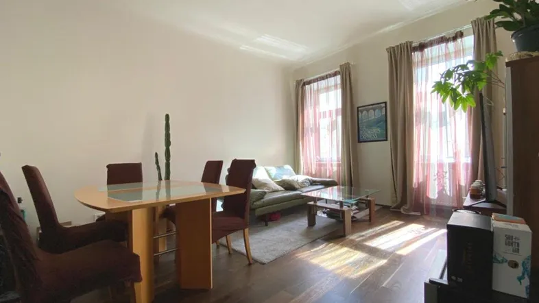 Helles Wohn- und Esszimmer mit dunklem Holzboden, modernem Sofa und Esstisch, durchflutet von natürlichem Licht.