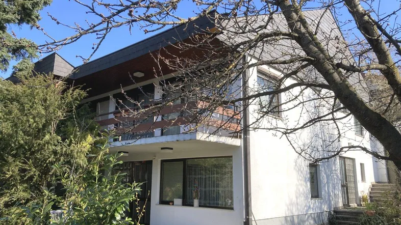 Weißes Einfamilienhaus mit Balkon und Gartenbereich unter blauem Himmel.