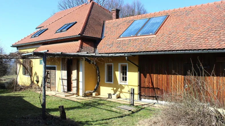 Gelbes Landhaus mit rotem Ziegeldach und Solarpaneelen auf dem Dach.