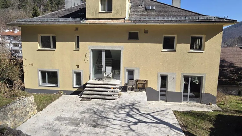 Geräumige Terrasse hinter dem Haus mit Zugang zu mehreren Räumen und Blick auf die bewaldeten Hügel.