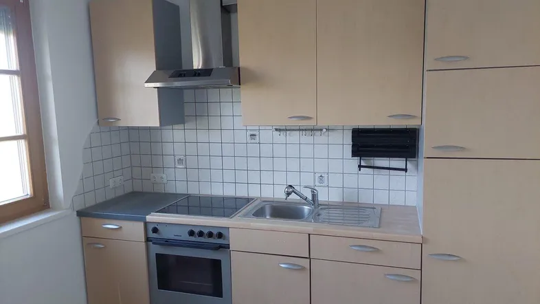Helle Einbauküche mit Holzfronten, Fliesenrückwand und Fenster für Tageslicht.