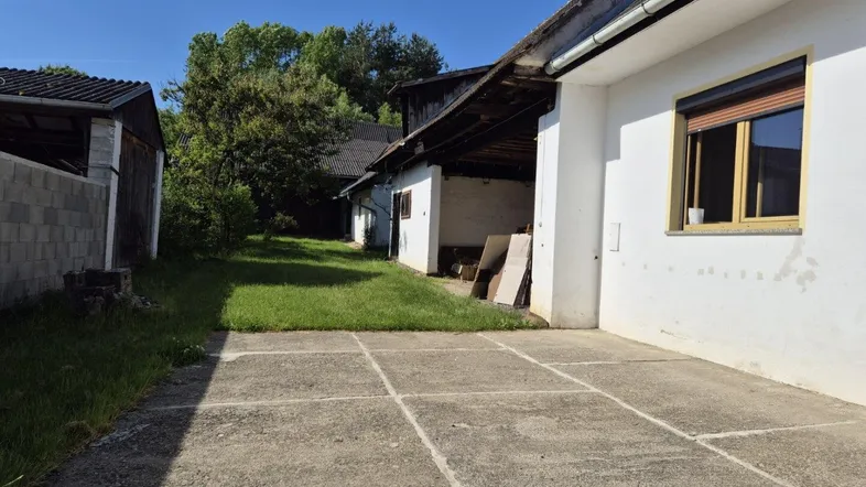 Betonierter Vorplatz mit weißer Gebäudefassade und Blick auf weitere ländliche Gebäude im Grünen.