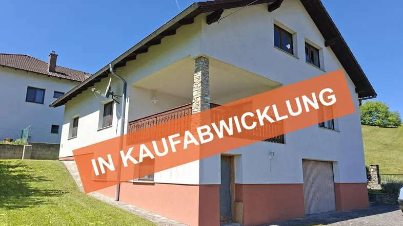 Einfamilienhaus mit weißer Fassade, Satteldach, Balkon und integrierter Garage in ländlicher Umgebung.