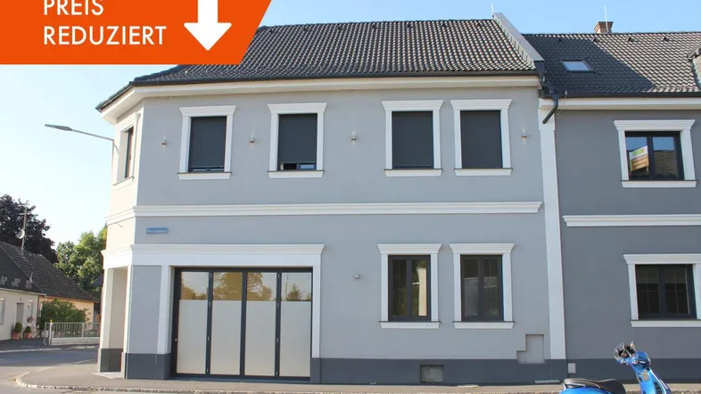 Modernisiertes Eckgebäude mit grauer Fassade, weißen Fensterumrandungen und dunklen Rollläden an einer städtischen Kreuzung.