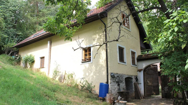 Traditionelles Landhaus mit Putzfassade und Holztüren, umgeben von viel Grün und Bäumen.