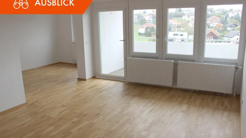 Helles Zimmer mit Parkettboden, großen Fenstern und Zugang zu einem Außenbereich mit Blick ins Grüne.