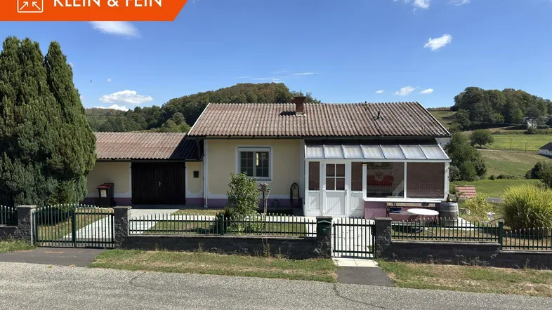 Einfamilienhaus mit Wintergarten und Vorgarten in ländlicher Umgebung unter blauem Himmel.