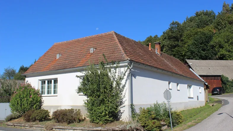 Seitenansicht des Hauses mit traditionellem Ziegeldach und umgebender Natur.