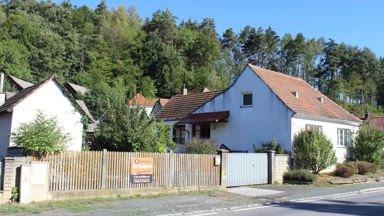 Weißes Einfamilienhaus mit rotem Ziegeldach, umgeben von Bäumen und einem Holzzaun.