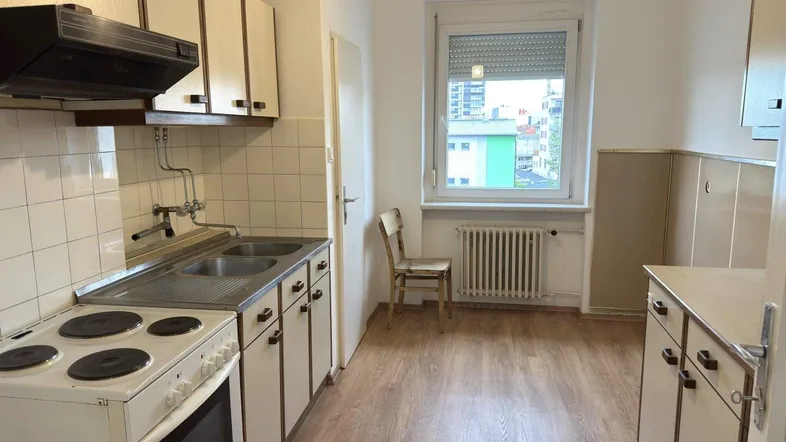 Einfache Küche mit älteren Einbauschränken, Herd und Spüle, bereit für eine Modernisierung.