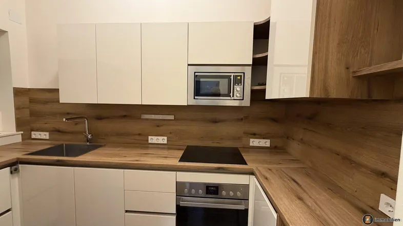 Moderne Küche mit weißen Hochglanzfronten, Holzoptik-Arbeitsplatten und integrierten Geräten.