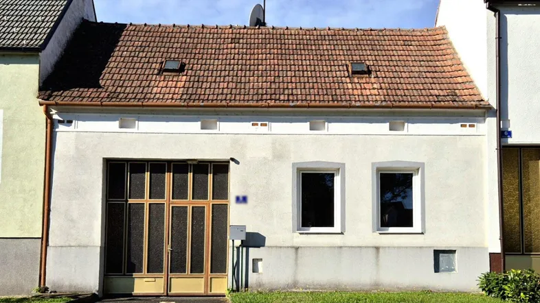 Vorderansicht eines Hauses mit Ziegeldach, zwei Fenstern und einem großen Garagentor.