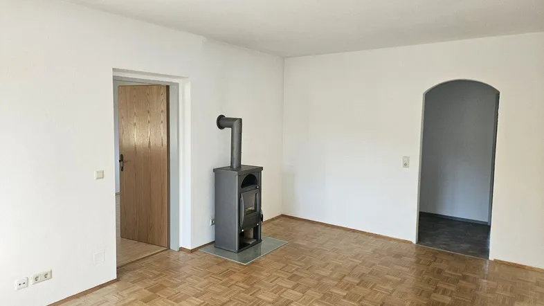 Helles Wohnzimmer mit Parkettboden und einem modernen Holzofen als Wärmequelle.