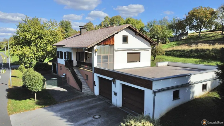 Freistehendes Einfamilienhaus mit Doppelgarage und großer Dachterrasse in ländlicher Umgebung.