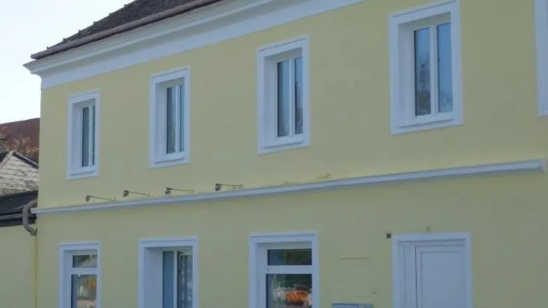 Gebäudefassade in hellem Gelb mit weißen Fenstern und klassischer Architektur.