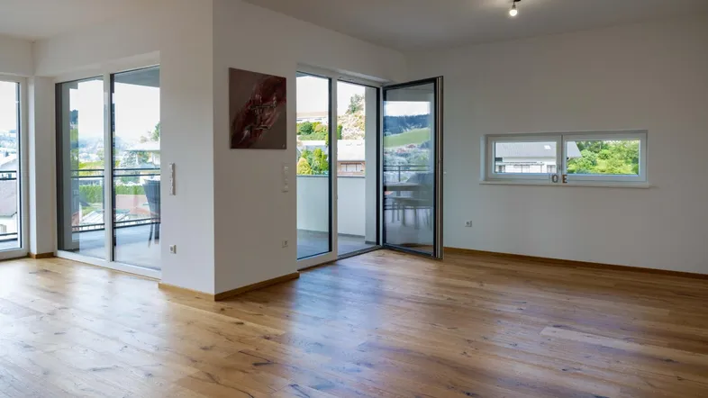 Helles Wohnzimmer mit Holzboden und Zugang zu einem Balkon, bietet einen weiten Blick.