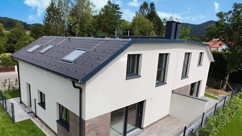 Modernes Einfamilienhaus mit heller Fassade, dunklem Dach und einer Terrasse im Grünen.