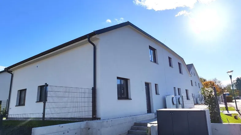 Moderne Doppelhaushälfte mit weißer Fassade, gepflastertem Eingangsbereich und blauem Himmel.