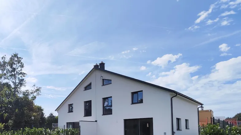 Modernes Einfamilienhaus mit weißer Fassade und Satteldach unter blauem Himmel.