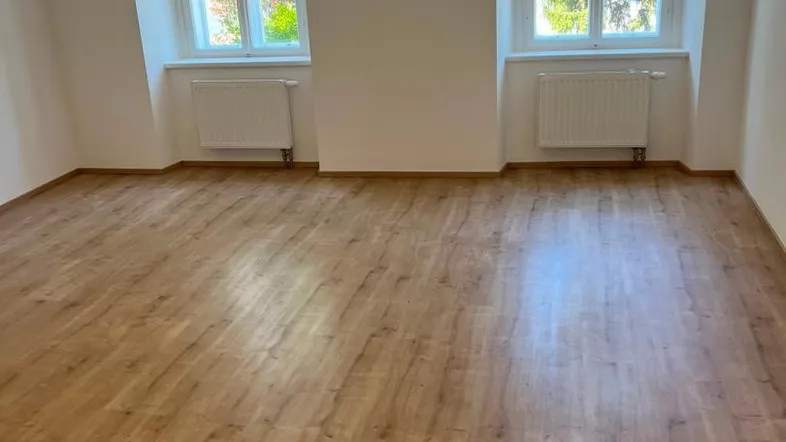 Helles Zimmer mit zwei Fenstern, Laminatboden und weißen Wänden, bereit zur individuellen Gestaltung.