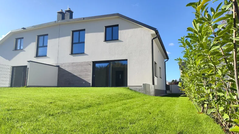 Modernes Einfamilienhaus mit weißer Fassade, großen Fenstern und gepflegtem Rasen unter blauem Himmel.