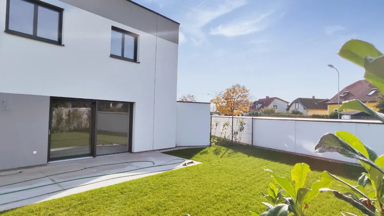 Moderne Hausfassade mit weißem Putz, grauen Akzenten und einem frisch angelegten Garten.