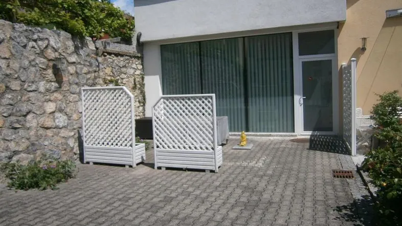 Gepflasterte Terrasse vor dem Gebäude mit großen Fenstern und einer Steinmauer im Hintergrund.