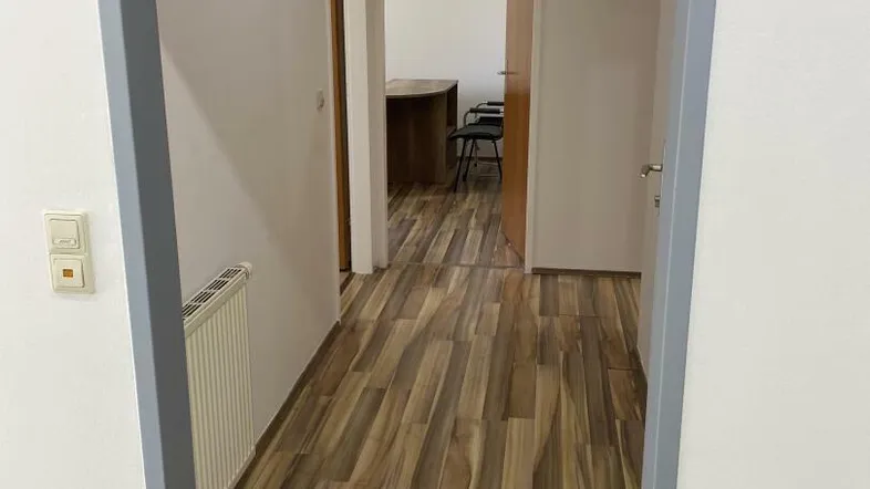 Langer Flur mit Laminatboden und weißen Wänden, der zu einem weiteren Raum führt.