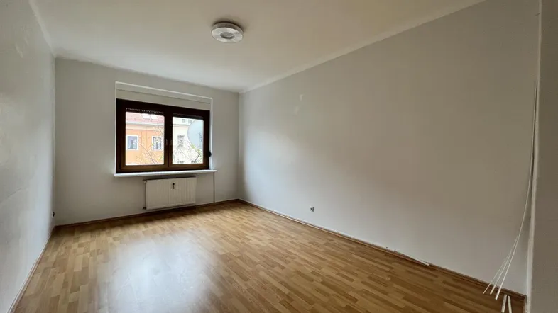 Heller, leerer Raum mit Laminatboden und einem Fenster, das Tageslicht hereinlässt.
