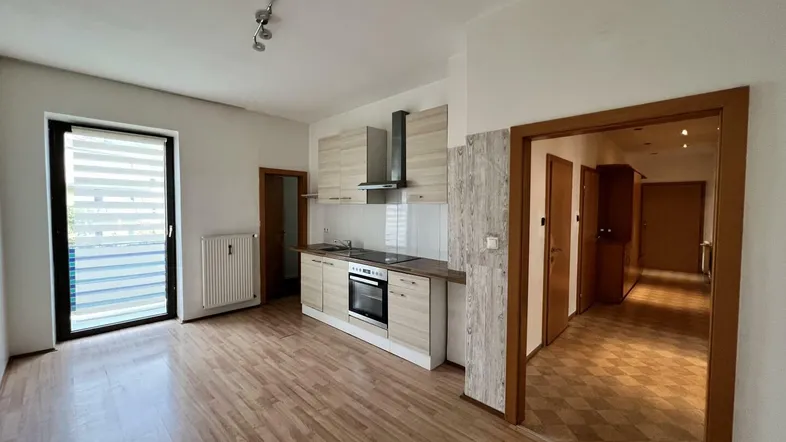 Heller offener Wohnbereich mit integrierter Küchenzeile und Zugang zum Balkon.