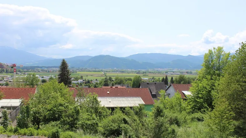 Weitläufiger Blick über Dächer, grüne Felder und eine Bergkette am Horizont unter blauem Himmel.