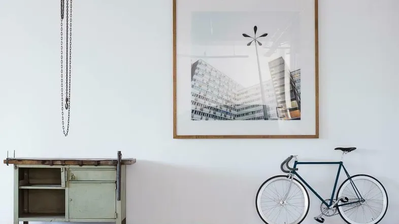 Heller Raum mit hoher Decke, einer Werkbank, einem Fahrrad und einem großen gerahmten Bild.