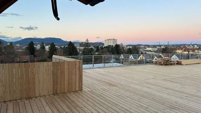 Weitläufige Holzterrasse mit Panoramablick über die Stadt bei Sonnenuntergang.