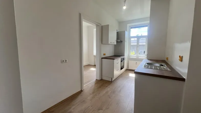 Helle Küche mit Laminatboden, Fenster und vorbereiteten Anschlüssen für weitere Geräte.